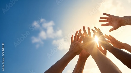 Diverse hands reaching up towards a bright sun in a clear blue sky, symbolizing unity and aspiration.