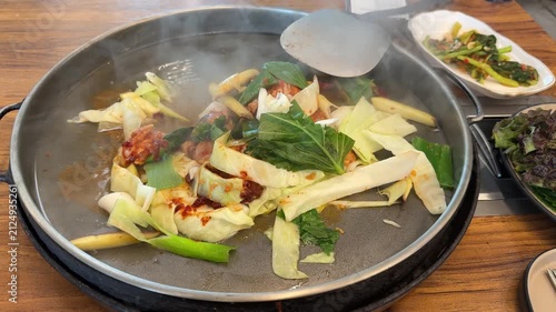 Ingredients of dakgalbi from Chuncheon on a flat pan at a restaurant. Chicken, cabbage, spring onion, tteok or rice cake, leafy greens and gochujang sauce ready to be cooked