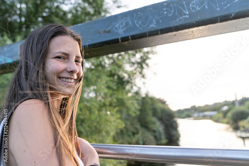 Fotografie Young woman smiling on bridge enjoying nature at sunset