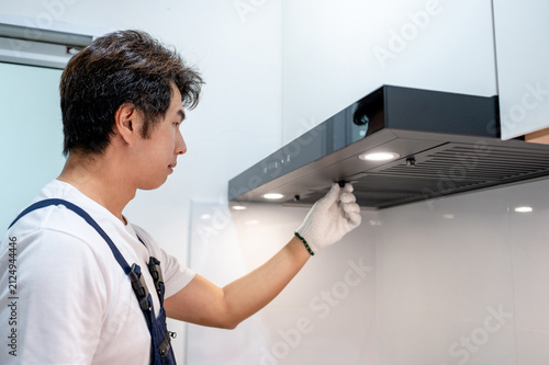 Asian male maintenance worker repairing modern cooker hood in domestic kitchen. Technician man wearing gloves cleaning kitchen range hood filter for clear ventilation. Home appliance service on site
