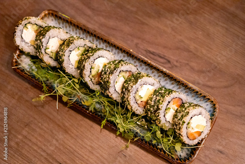 Long plate of Philadelphia sushi rolls coated with sesame seeds on wooden table. Japanese sushi concept for restaurant dining and Asian food culture.