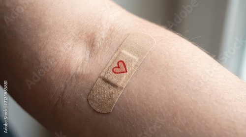 Closeup of small adhesive bandage with red heart on inner arm after blood donation for world blood donor day poster background and volunteer awareness