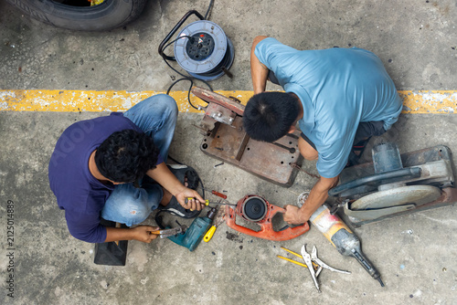 Photography Top view of two mechanics repairing dissembled power tools on concrete floor
