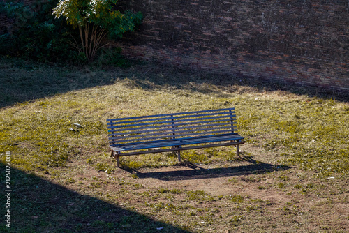 Fotografie Rome, Italy – November 11, 2025: Empty park bench in sunlight beside old brick w