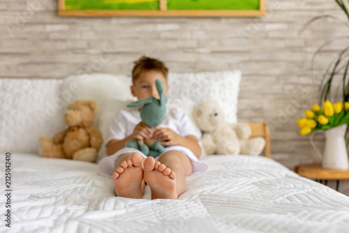 Cute little preschool child, cute blond boy, playing in bed with many teddy bears, handmade amigurumi toys, enjoying toy game