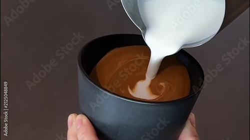Barista pouring milk for heart rosette latte art in black cup