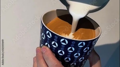 Barista pouring milk for heart rosette latte art in patterned ceramic cup