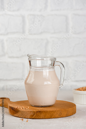 Plant-based green buckwheat milk served in pitcher on white kitchen background. Vertical orientation.