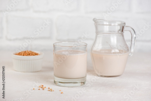 Fresh vegan buckwheat milk in glass with raw grains, plant-based nutrition concept