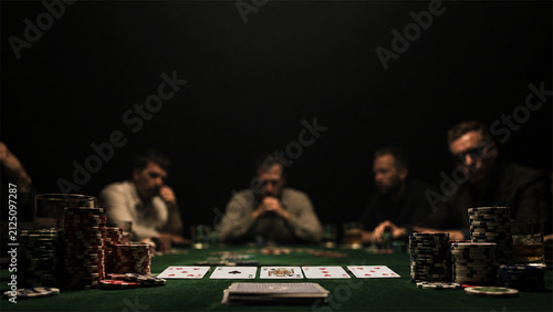 Group of friends seated around a green poker table in a dark private room with cards and chip stacks creating a cinematic game night scene focused on strategy competition and social leisure