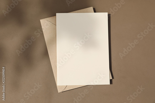 Fotografía Blank greeting card mockup with kraft envelope on neutral brown table textured background in warm natural sunlight, shadows