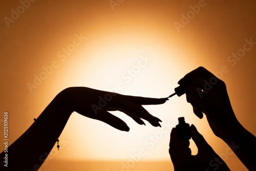 Silhouette of Hands Painting Fingernails with Nail Polish Against a Warm Blurred Background