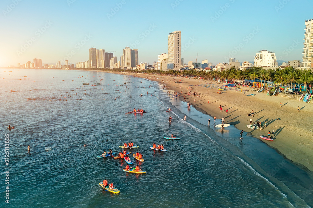 Obraz premium Beachgoers swim and paddle on paddleboards and surfboards in the vibrant blue ocean along Da Nang busy shoreline