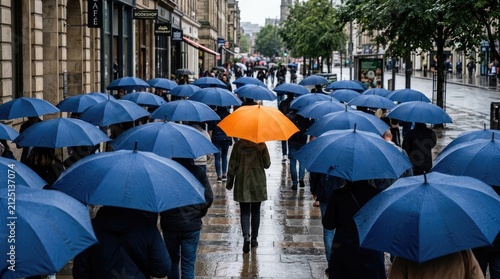 A large group of people walks down a city street during a heavy rainstorm. Many individuals are holding blue umbrellas, creating a sea of blue.