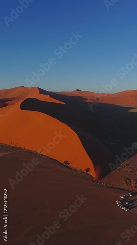 Red dunes of Sossusvlei, Namibia. Aerial view along a towering sand ridge with hikers small against the sunlit slope.