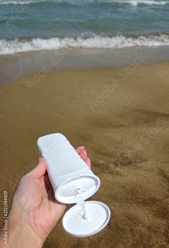 White sunscreen tube on golden beach sand near the ocean waves. High quality photo
