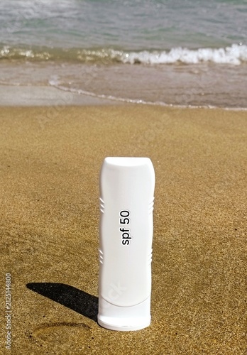 White sunscreen tube on golden beach sand near the ocean waves. High quality photo