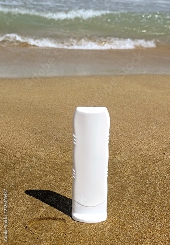 White sunscreen tube on golden beach sand near the ocean waves. High quality photo