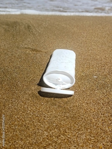 White sunscreen tube on golden beach sand near the ocean waves. High quality photo