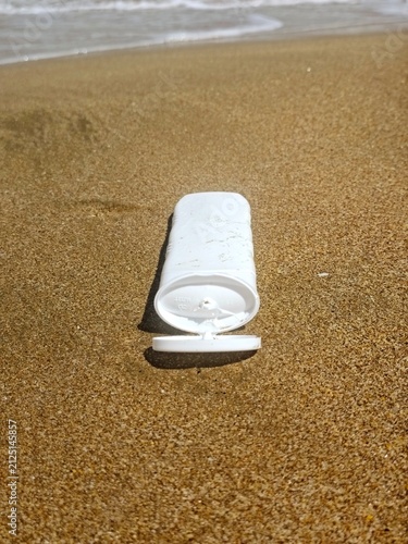 White sunscreen tube on golden beach sand near the ocean waves. High quality photo