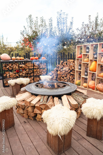 Fire pit in outdoor area surrounded by wooden logs and fresh vegetables on display