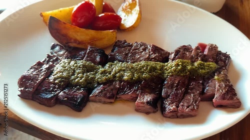 Sliced skirt steak served with chimichurri sauce roasted potatoes and cherry tomatoes. Gourmet grilled beef dish with traditional Argentine flavors presented in a restaurant. High quality 4k footage
