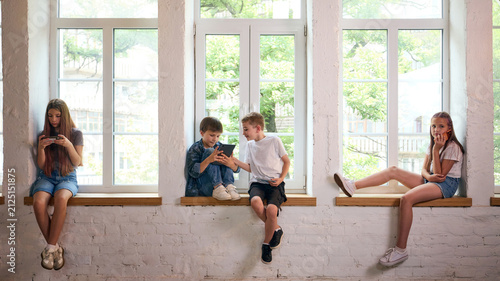 фотографія Children absorbed in smartphones and tablet while sharing bright window seat