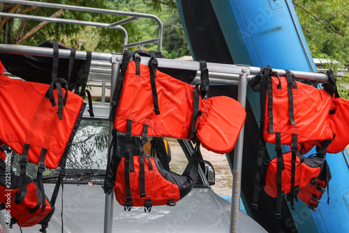 Bright orange life jacket hanging on metal rack above vehicle next to inflatable blue raft, outdoor river rescue gear ready for water adventure