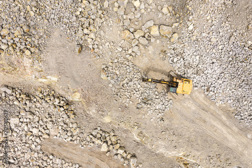 Aerial top down view of a yellow excavator working in a stone quarry, heavy machinery digging rocks in an open pit mine