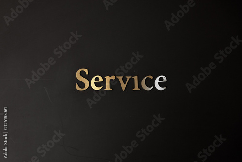 Gold metallic word Service on a dark black wall background. Business customer care, hospitality, help desk, and support concept.