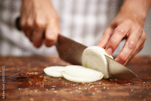 Chef slicing onion on wooden cutting board