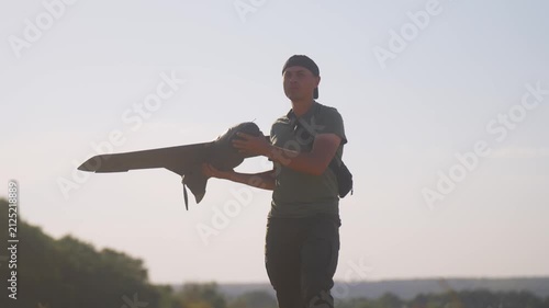 man UAV pilot with plane drone in hands preparing to launch drone in field at summer evening. warm sunset light and sun flares in frame. technology and engineering in modern warfare.