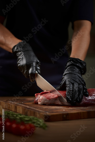 Butcher hands cutting raw beef steak on board