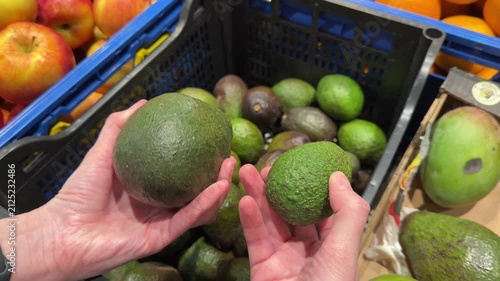 Comparing Sizes of Two Avocados Held in Hands at Grocery Store