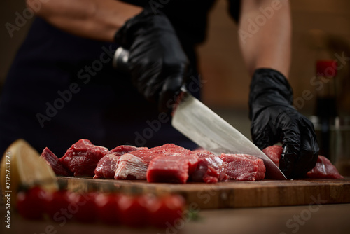 Chef hands slicing raw beef on cutting board