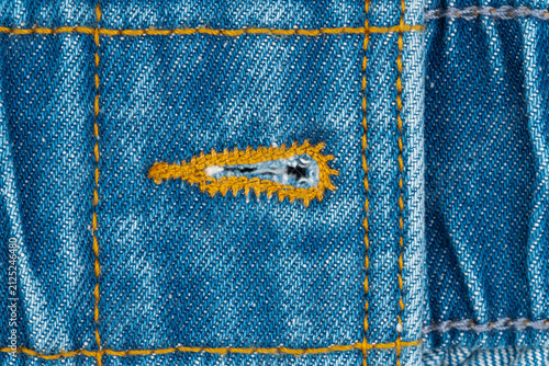 Foto Denim fabric closeup with buttonhole, yellow stitching and small tear repair but
