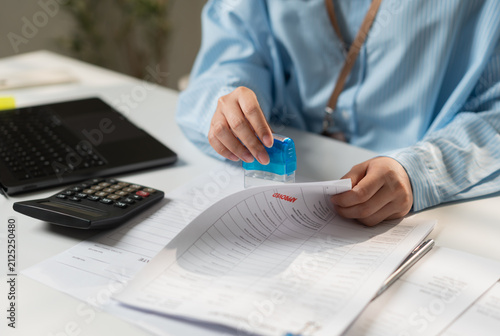 Businesswoman stamping approved financial documents with calculator and laptop in a modern office, representing document approval, accounting, tax compliance, auditing and administrative workflow.