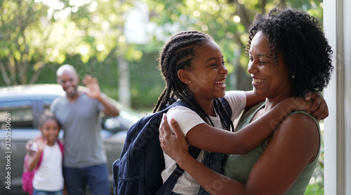 A daughter hugs her mother goodbye for Back to School at home, showing happy family child parent education with student school supplies