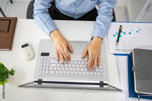 Woman analyzes charts on a laptop. She studies data with focused intent. Desk holds plants, notes, and a phone. Professional workspace with soft lighting
