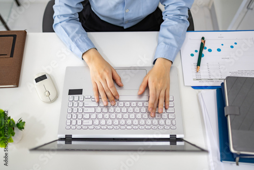 Woman analyzes charts on a laptop. She studies data with focused intent. Desk holds plants, notes, and a phone. Professional workspace with soft lighting
