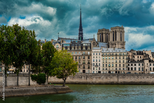 Notre-Dame Cathedral stands among typical parisian buildings under a dramatic sky in Paris, France.