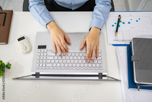 Woman analyzes charts on a laptop. She studies data with focused intent. Desk holds plants, notes, and a phone. Professional workspace with soft lighting
