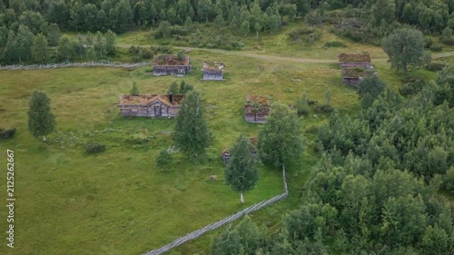 Aerial view of Storklappvallen featuring traditional wooden cabins with grass roofs set in a lush green meadow surrounded by forest in Bruksvallarna, Jamtland County, Sweden.
