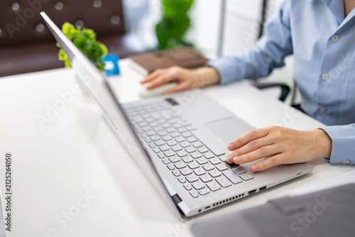 Woman analyzes charts on a laptop. She studies data with focused intent. Desk holds plants, notes, and a phone. Professional workspace with soft lighting
