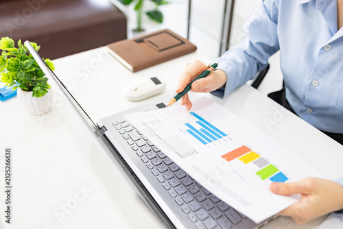 Woman analyzes charts on a laptop. She studies data with focused intent. Desk holds plants, notes, and a phone. Professional workspace with soft lighting
