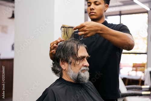 Foto Barber cutting hair for mature male customer