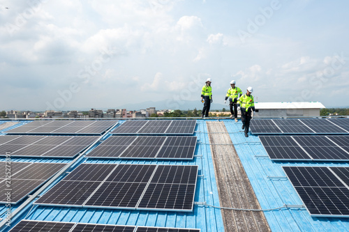 Aerial view of technicians installing solar panels on blue roof. Engineers maintaining solar energy system on a building rooftop. Top down view of workers in orange uniform fixing solar panels. 