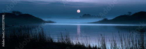 nocturnal lake with full moon over misty horizon, peaceful blue hour landscape with moonlight reflection on calm water, serene night waterscape with lavender sky and natural hills
