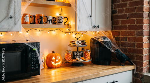 Office coffee corner with Halloween theme. mugs, treats, subtle web decor, warm lighting.
