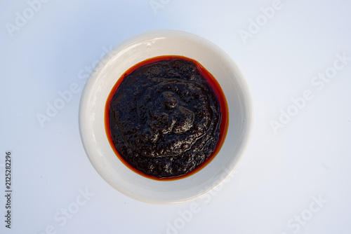 Thai roasted chili paste (Nam Prik Pao) served in a small white bowl, top view isolated on white background